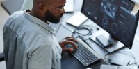 Minimal high angle view at African American software developer working with computers and data systems in office