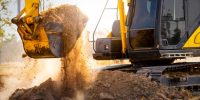 Close-up of excavator at construction site. Backhoe digging soil for earthwork and construction business. Excavating machine at work. Heavy machinery for earth moving and construction site development